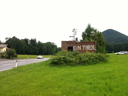 eine ruine an einer straße, auf in riesigen lettern "ein tirol" gesprüht ist